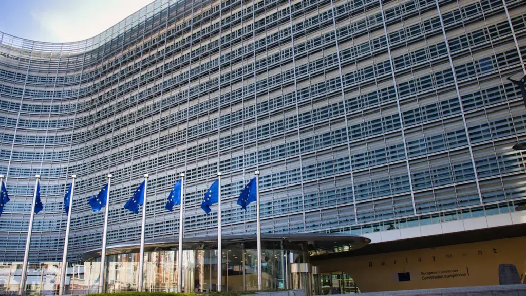 Moderni Europos Komisijos pastato architektūra su plazdančiomis Europos Sąjungos vėliavomis Briuselyje.
