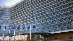 Moderni Europos Komisijos pastato architektūra su plazdančiomis Europos Sąjungos vėliavomis Briuselyje.