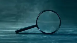 Didelis didinamasis stiklas tamsiame fone, simbolizuojantis vidinį tyrimą dėl interesų konflikto.