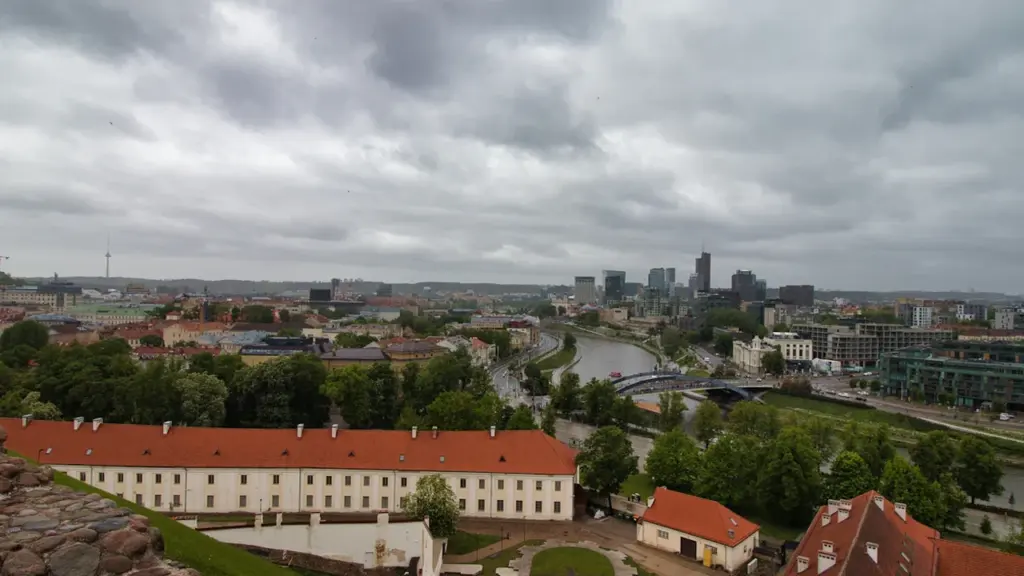 Vilniaus miesto panorama su debesuotu dangumi, nusitęsusi per horizontą virš upės.