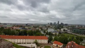 Vilniaus miesto panorama su debesuotu dangumi, nusitęsusi per horizontą virš upės.