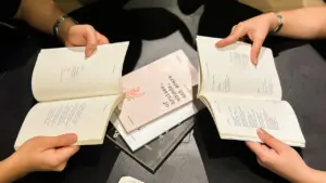Žmonės prie stalo skaito knygas, simbolizuojančias konstitucinius teisinius dokumentus bei pilietinį ugdymą.